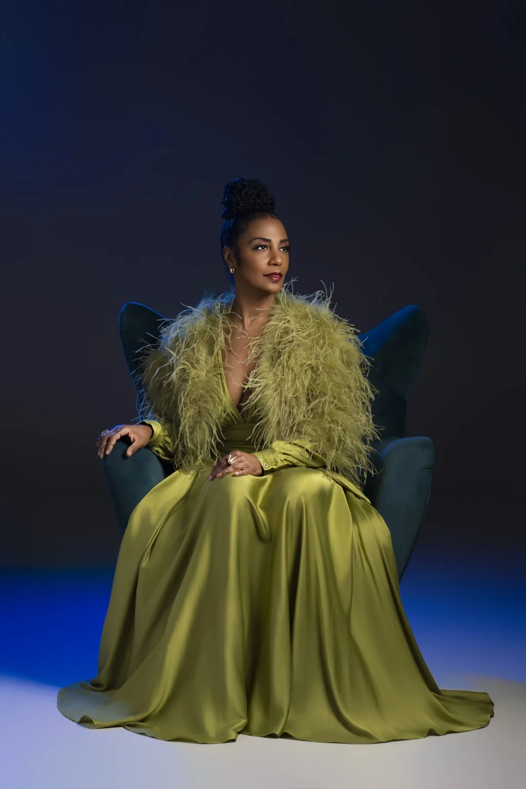 Yvette Spears seated in an olive-green gown and feathered wrap